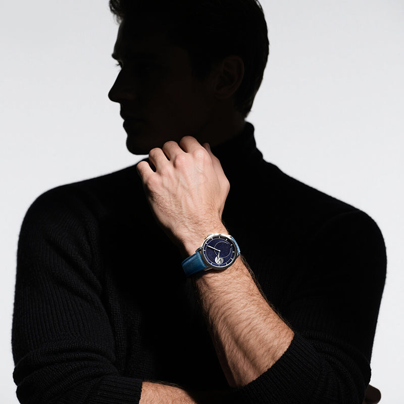 Male model wearing Agelocer Astronomer aventurine moonphase watch with blue leather strap, studio lifestyle shot