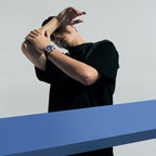Agelocer Baikal blue dial watch worn by a male model with arms raised in a studio editorial shot