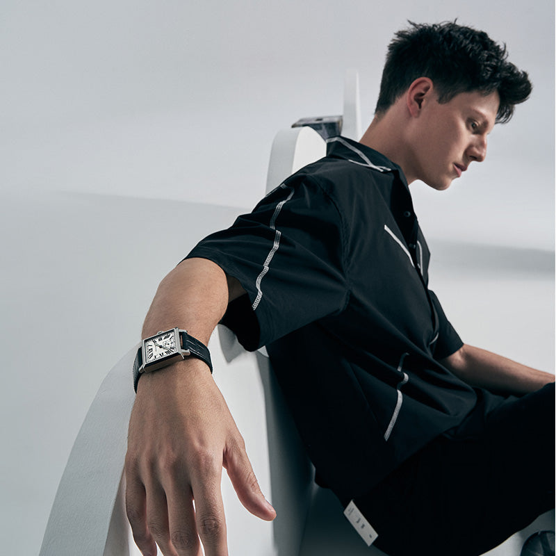Male model wearing Agelocer Codex square automatic watch with white Roman dial, seated lifestyle shot