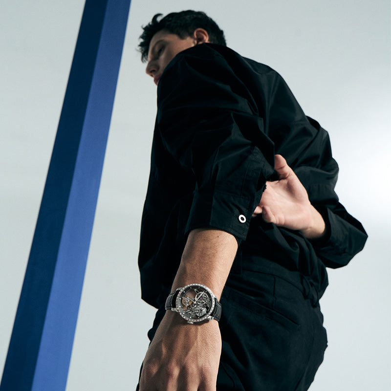 Man walking wearing Agelocer free-sprung diamond tourbillon watch on black leather strap, lifestyle shot