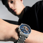 Agelocer Free-Sprung diamond tourbillon watch with blue dial and steel bracelet worn on the wrist, close-up