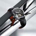 Agelocer flying tourbillon watch with steel case and black strap resting on polished steel bars, lifestyle
