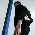 Male model wearing Agelocer Free-Sprung skeleton tourbillon watch with steel bracelet, dynamic lifestyle shot