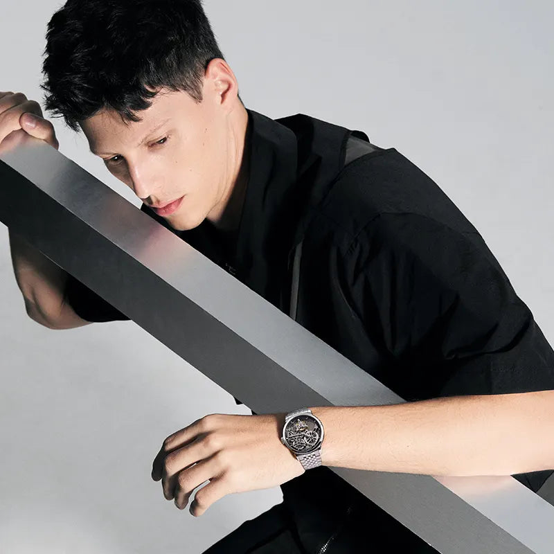 Male model wearing Agelocer flying tourbillon watch on steel bracelet, dynamic studio shot