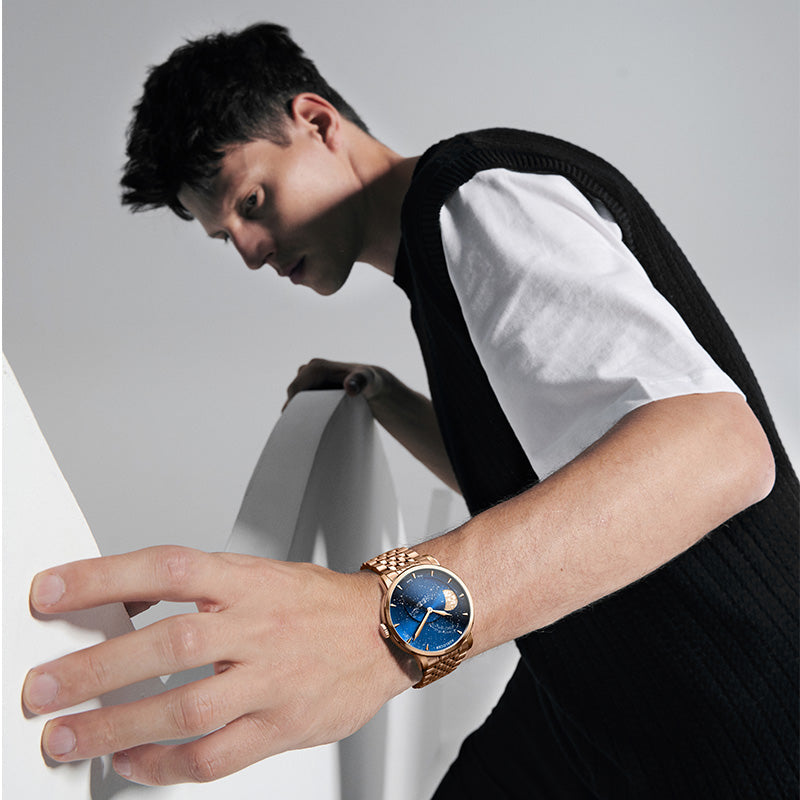 Agelocer Galaxy Astronomer Moonphase rose gold watch worn by a man leaning on a white plinth