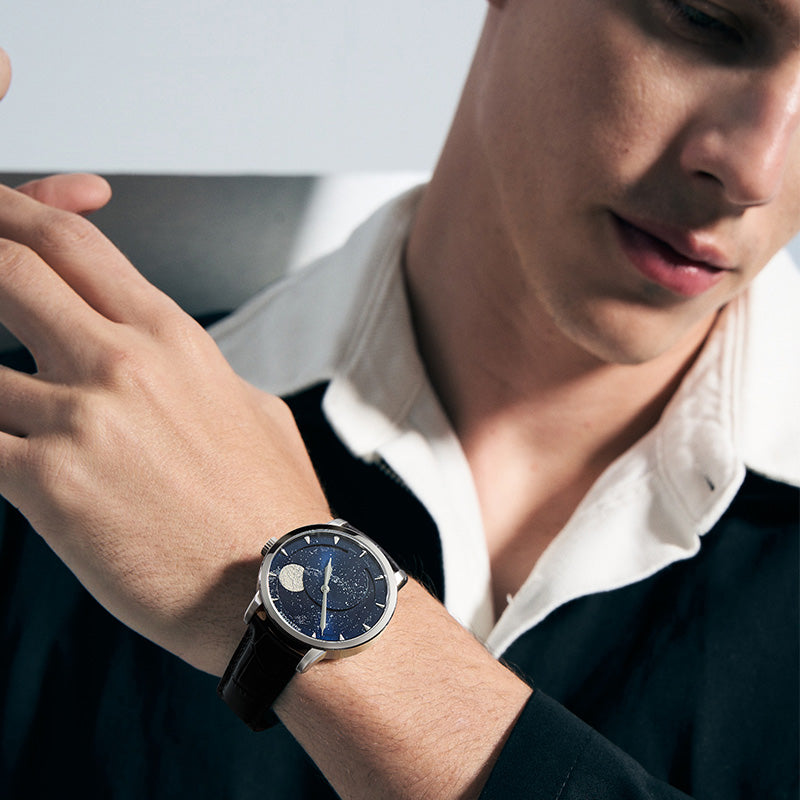 Man wearing Agelocer Astronomer galaxy moonphase watch, blue starry dial on brown strap, wrist view