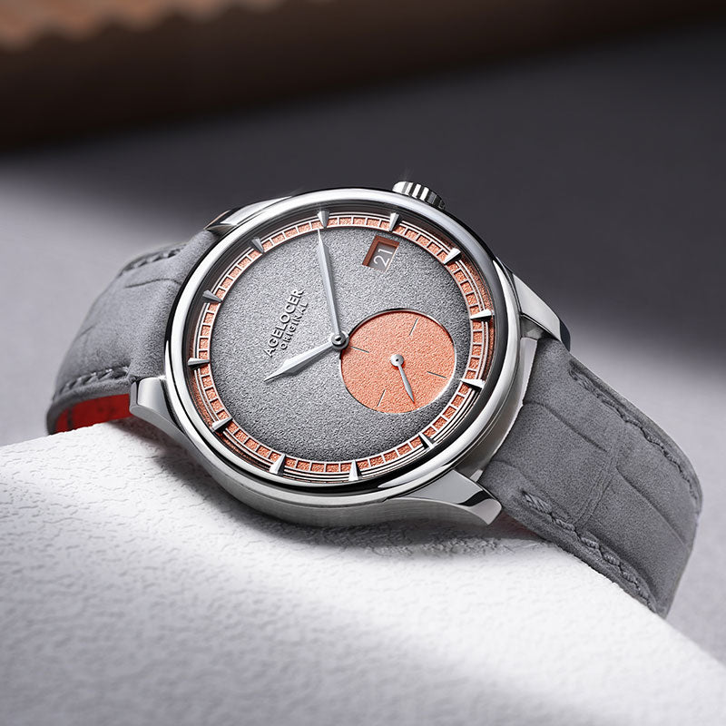 Agelocer Petite Seconde automatic watch with salmon accents on grey fabric, angled lifestyle shot