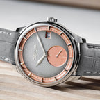 Agelocer Petite Seconde automatic watch on a wood surface, steel case with salmon sub-dial, lifestyle view