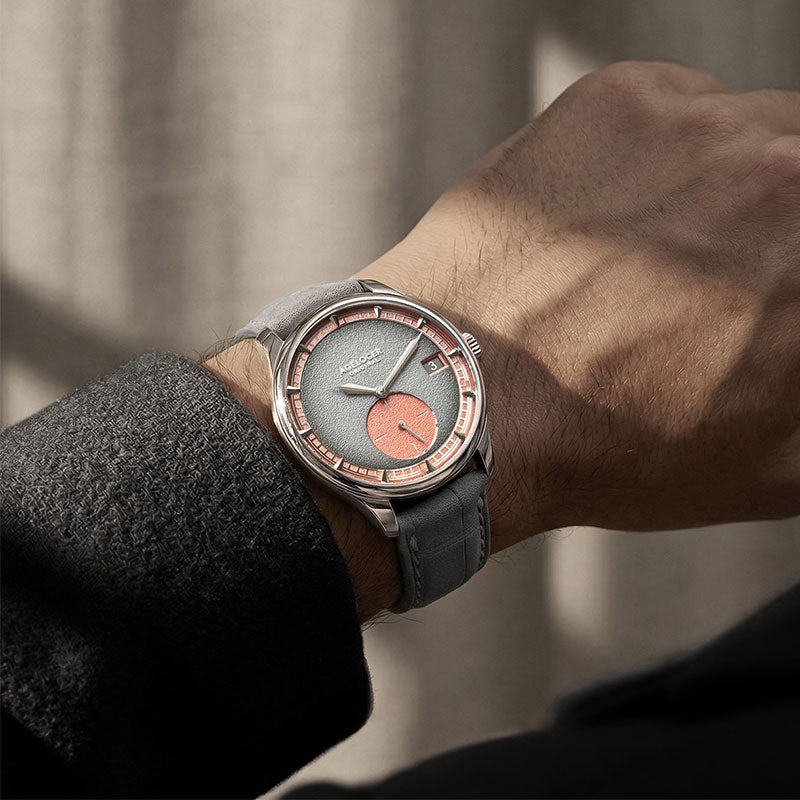 Man wearing Agelocer Petite Seconde automatic watch with salmon dial accents on grey strap, wrist view