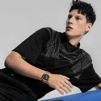 Male model wearing Agelocer Racing Square rose gold watch on steel bracelet, seated studio lifestyle shot