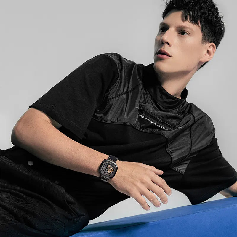 Male model wearing Agelocer Racing Square automatic watch on black leather strap, seated lifestyle shot