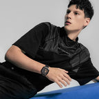 Male model wearing Agelocer Racing Square automatic watch on black leather strap, seated lifestyle shot
