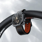 Agelocer Racing Square skeleton watch on a black leather strap resting on a car steering wheel, lifestyle
