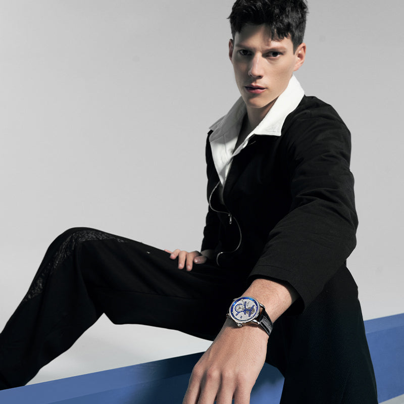 Male model wearing Agelocer Space Station automatic watch with blue dial, seated studio lifestyle shot