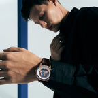 Man wearing Agelocer World Time watch with blue globe dial and rose gold case, wrist lifestyle shot