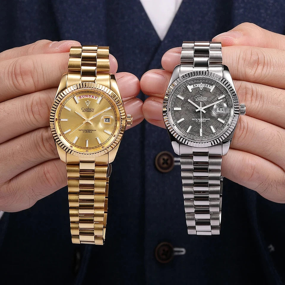 Two CADISEN C8214 watches, one gold with champagne dial and one silver with textured dial, held in hands against dark background