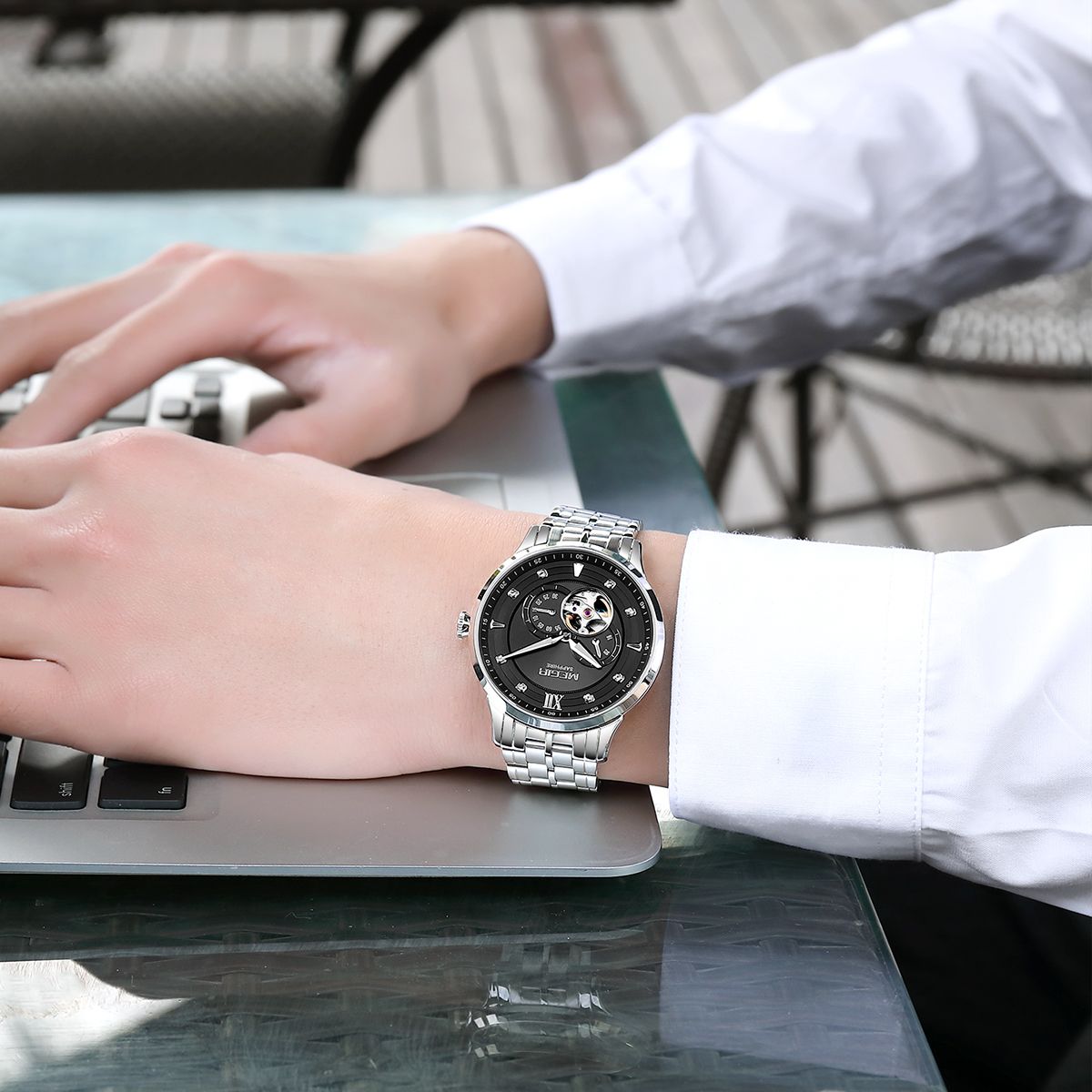 MEGIR 62053 automatic watch on the wrist, silver case and bracelet with black open-heart dial, at a laptop