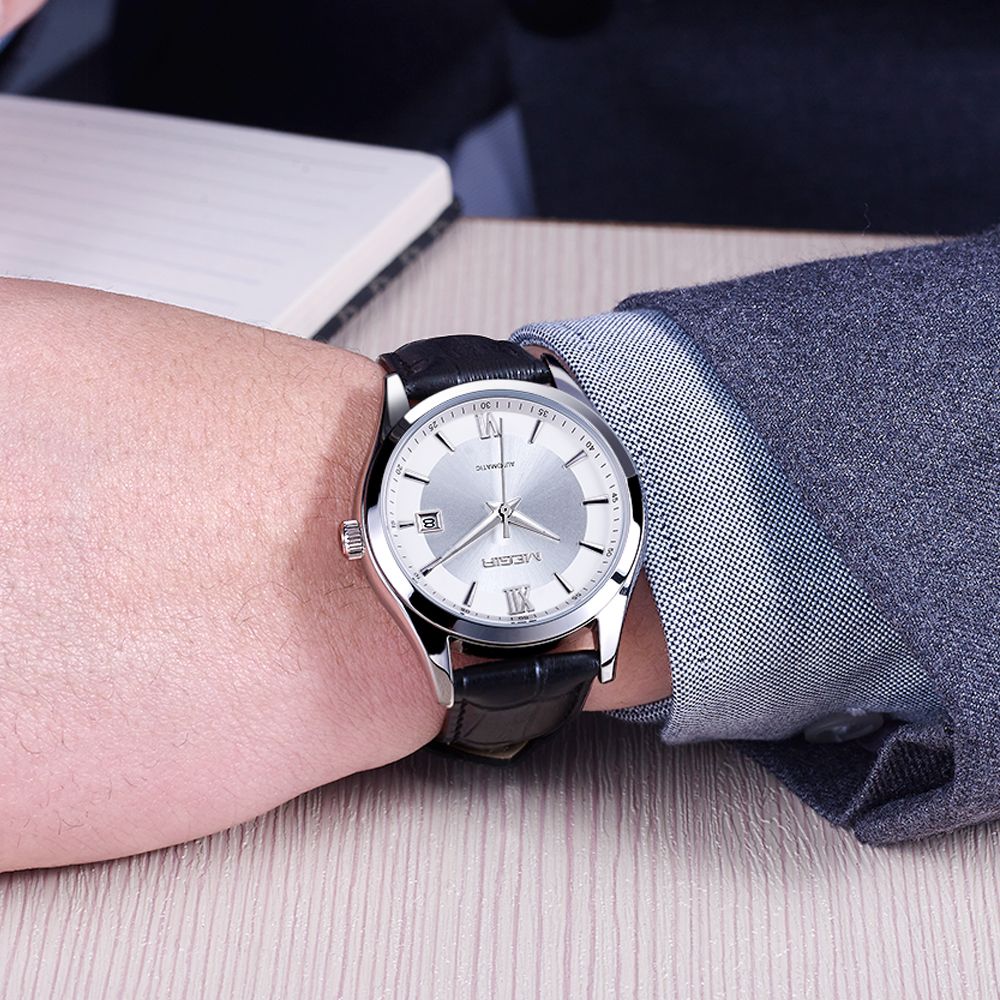 MEGIR 62063 automatic watch on the wrist, silver case, silver-white dial with date and black leather strap, at a desk