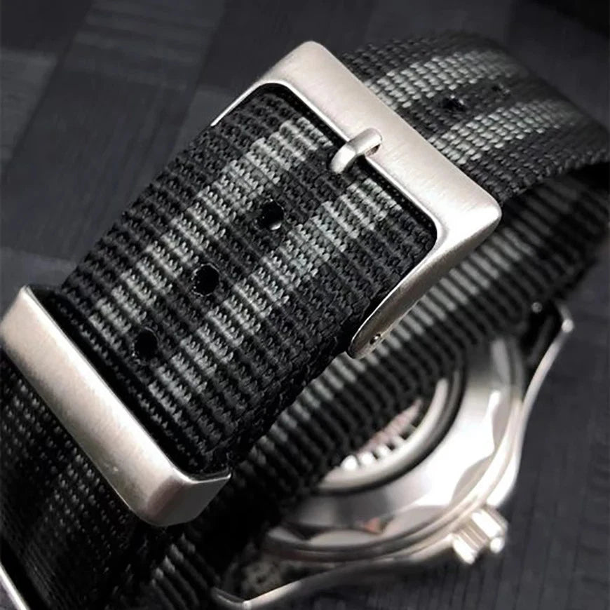 Close-up view of Pagani Design nylon watch strap with black and grey stripes and 20mm width, showing stainless steel buckle attached to a watch