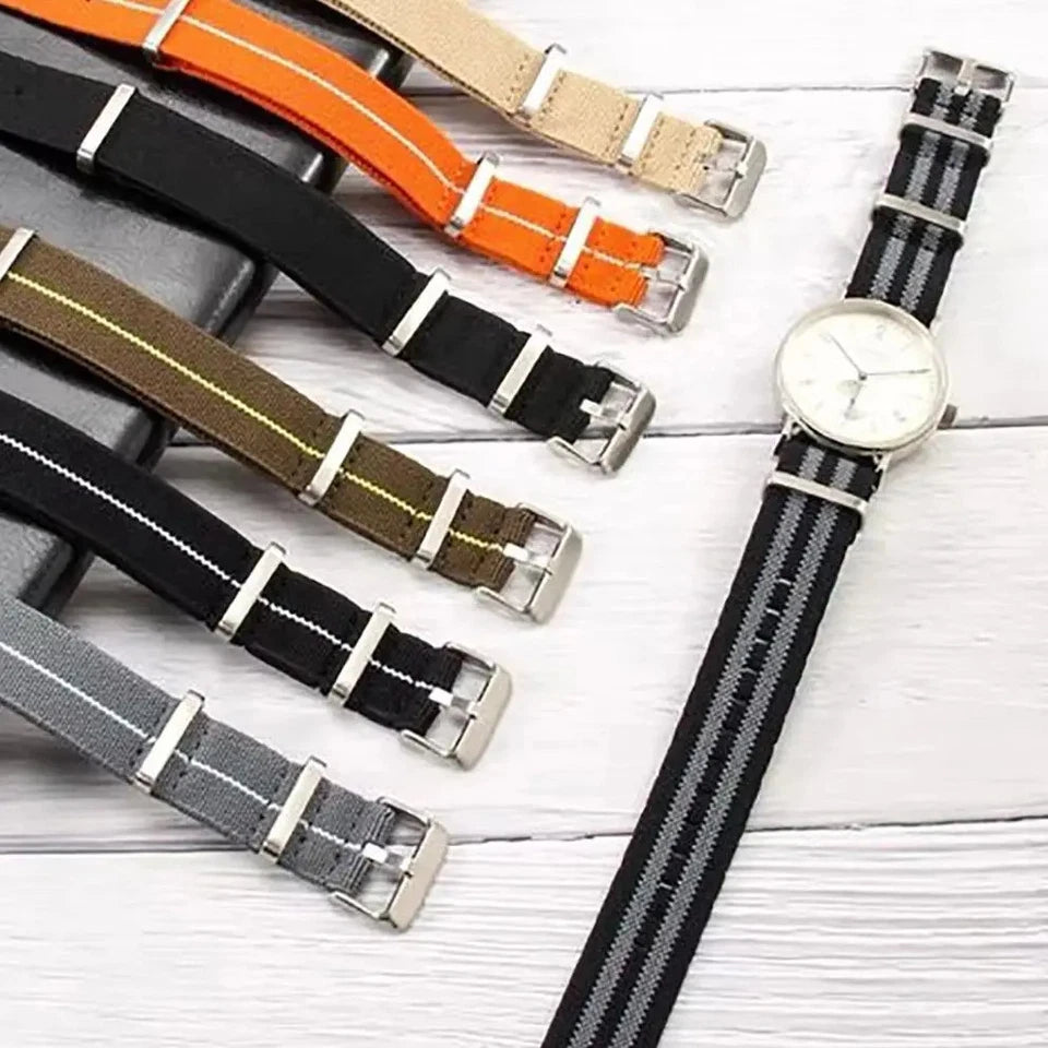 Collection of Pagani Design nylon watch straps in multiple colors including orange, beige, black, khaki, and grey, displayed alongside a watch on a wooden surface, 20mm width