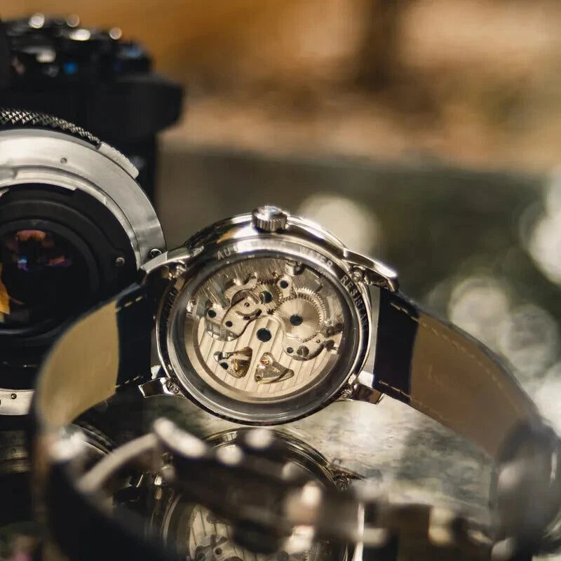 Caseback view of Pagani Design PD-1638 skeleton automatic watch with silver case and black leather strap, showcasing the mechanical movement and strap with blurred camera in background.