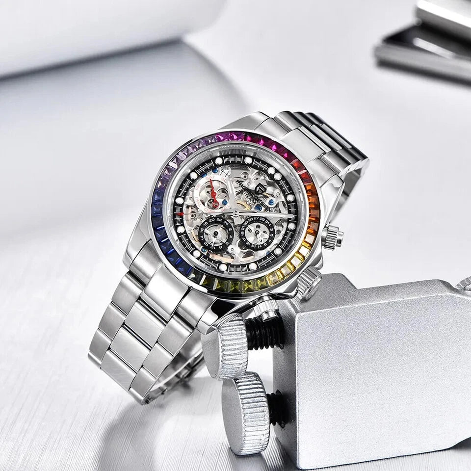 Lifestyle photo of Pagani Design PD-1653 automatic mechanical chronograph watch with skeleton dial, rainbow bezel, and polished stainless steel bracelet, positioned on a metal clamp against a light background.