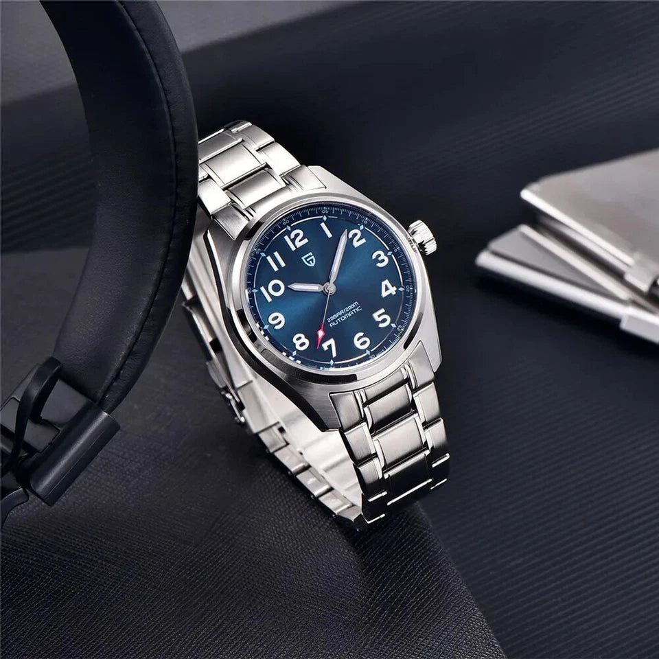 Lifestyle photo of Pagani Design PD-1717 automatic mechanical watch with blue dial and stainless steel bracelet, placed on a black surface with headphones and wallet.