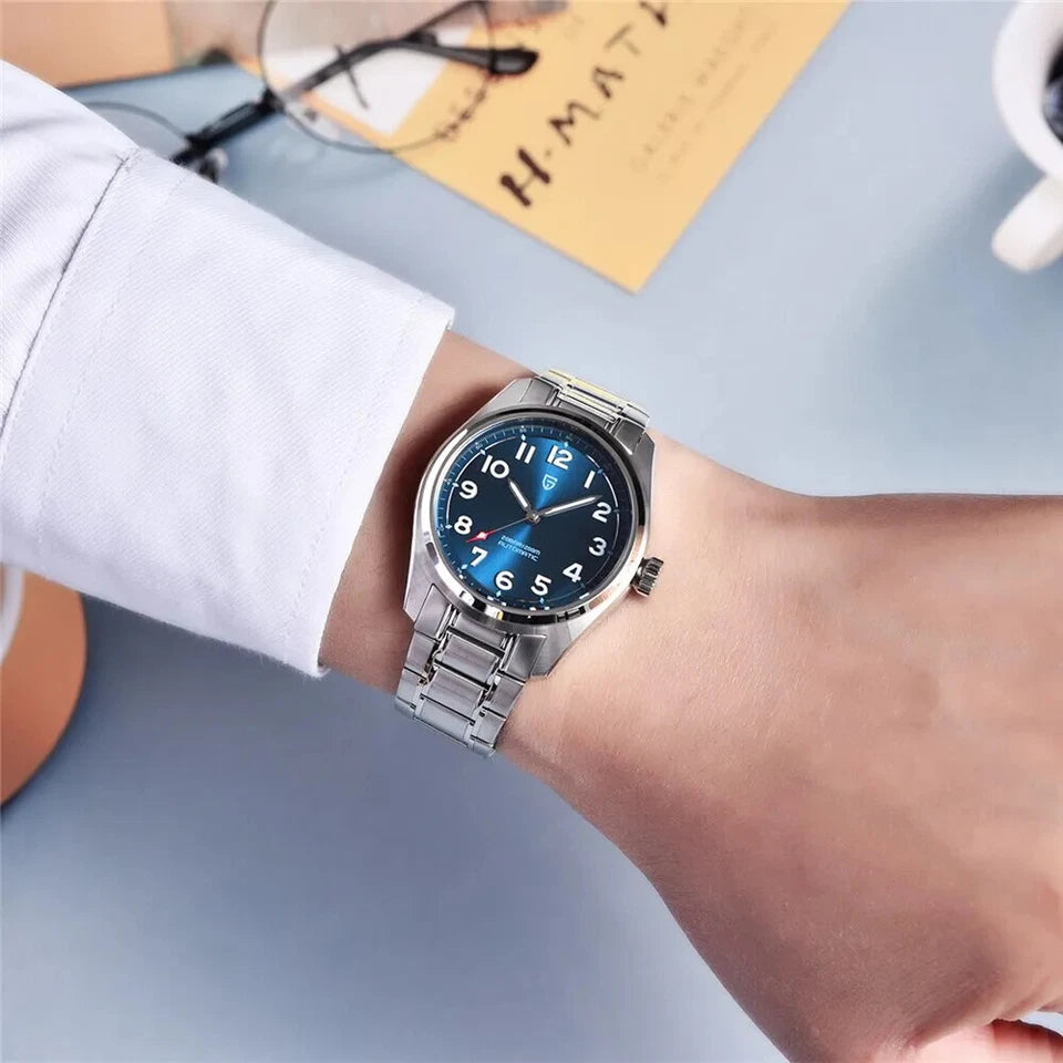 Wrist shot of Pagani Design PD-1717 automatic mechanical watch with blue dial and stainless steel bracelet worn on a wrist with white cuff and blue background.