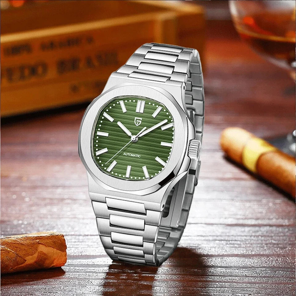 Lifestyle photo of Pagani Design PD-1728 mechanical automatic watch with green dial, stainless steel case and integrated bracelet, displayed on a wooden table with cigars and a glass in the background.
