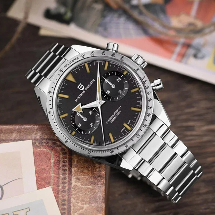 Lifestyle shot of Pagani Design PD-1766 men's moon quartz chronograph watch with a black dial, gold-tone markers, chronograph subdials, tachymeter bezel, stainless steel case, and matching stainless steel bracelet, placed on a rustic wooden surface with a blurred background.