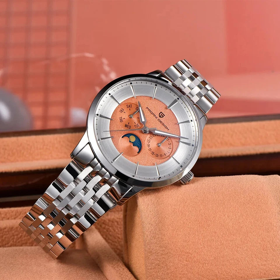 Lifestyle photo of Pagani Design PD‑1795 men's quartz watch with salmon dial, silver case, stainless steel bracelet, and moonphase display, resting on a tan watch cushion with a blurred pink background.
