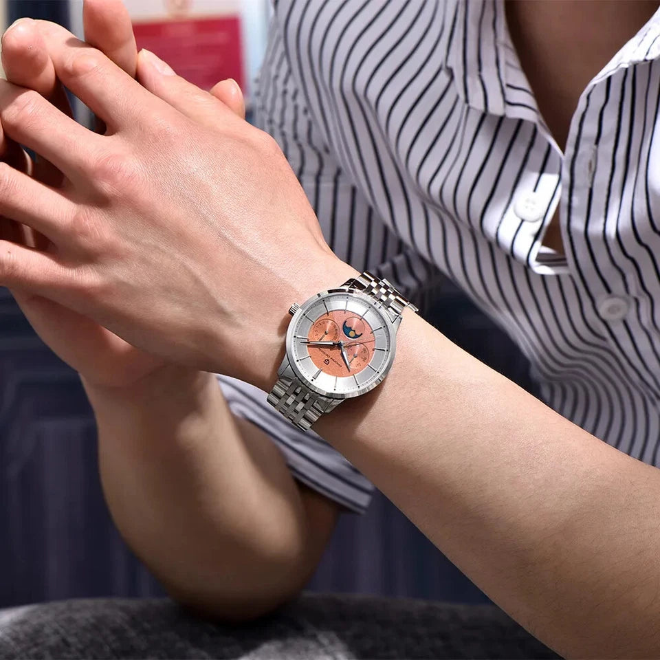 Wrist shot of Pagani Design PD‑1795 men's quartz watch with salmon dial, silver case, stainless steel bracelet, and moonphase display, worn on a wrist with a striped shirt and blurred background.