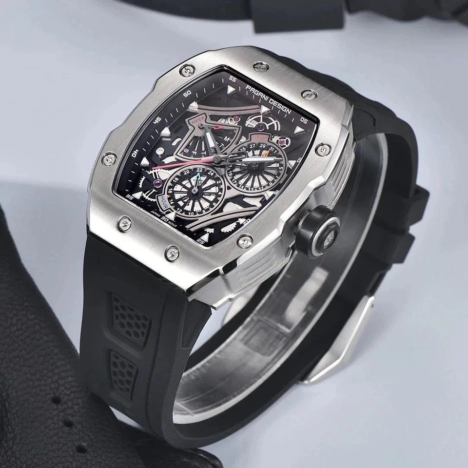 Lifestyle shot of Pagani Design PD‑YS012 skeleton sport watch with black rubber strap and silver tonneau case displayed on a light gray surface, showing the skeleton dial with chronograph subdials.