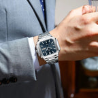 POEDAGAR 672 mens square waterproof watch with blue dial on wrist holding glass with grey suit