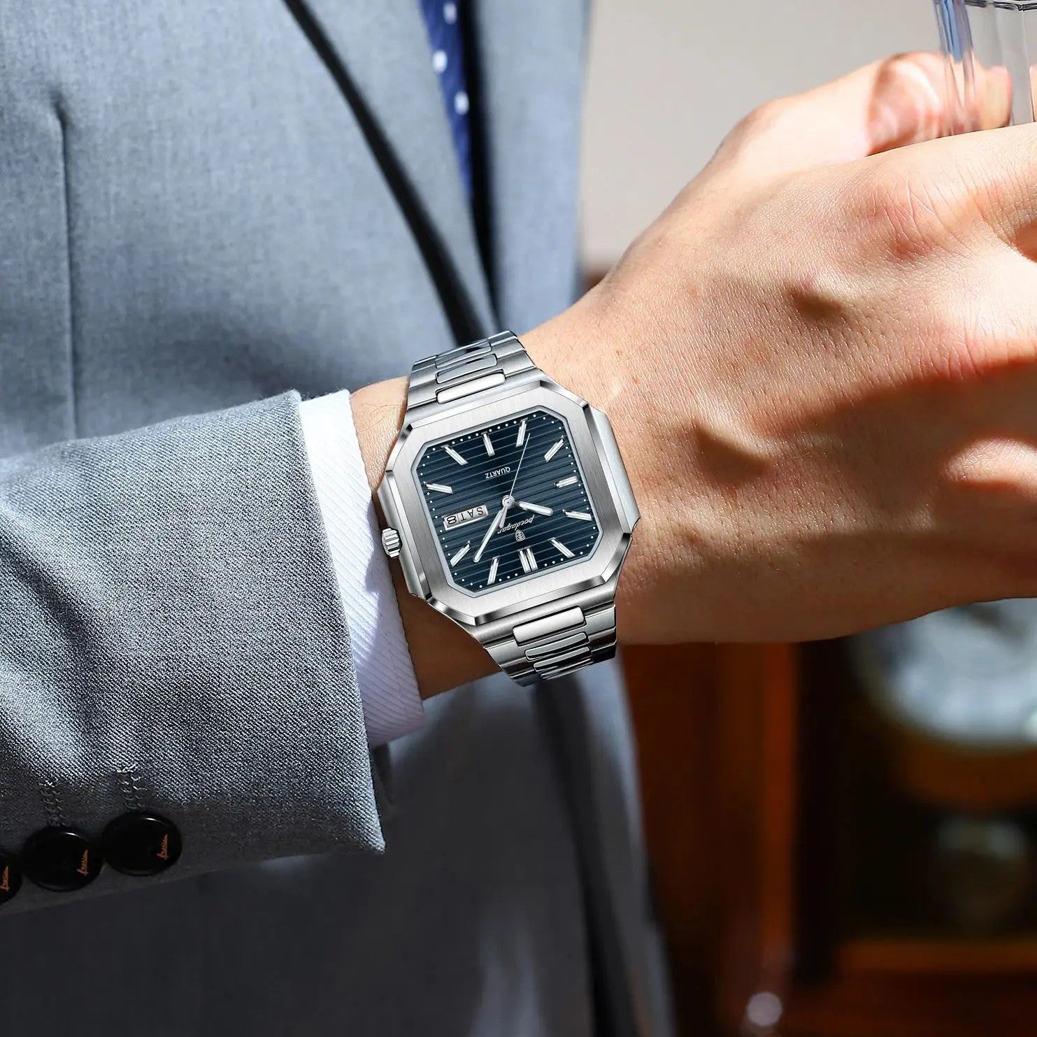 POEDAGAR 672 mens square waterproof watch with blue dial on wrist holding glass with grey suit