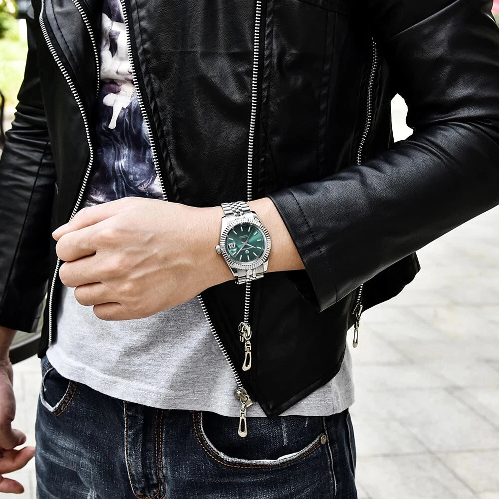 Person wearing a black leather jacket, gray shirt, and blue jeans with a silver watch on an outdoor background.