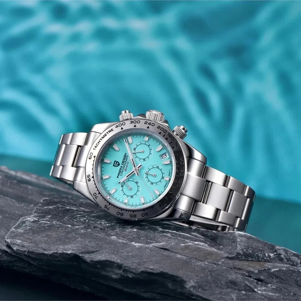Silver watch with a turquoise face on a dark rock with a blue water background