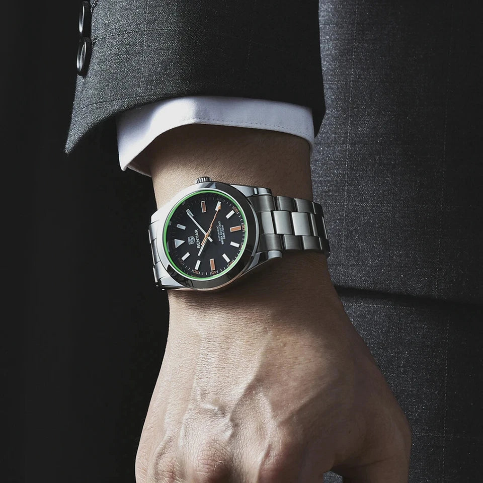 Silver watch with a green face on a person's wrist, wearing a suit.