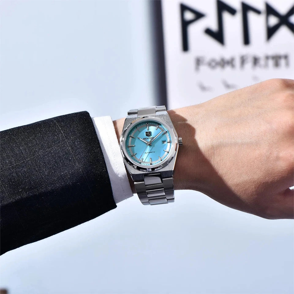 Hand wearing a silver watch with a blue face, blurred background