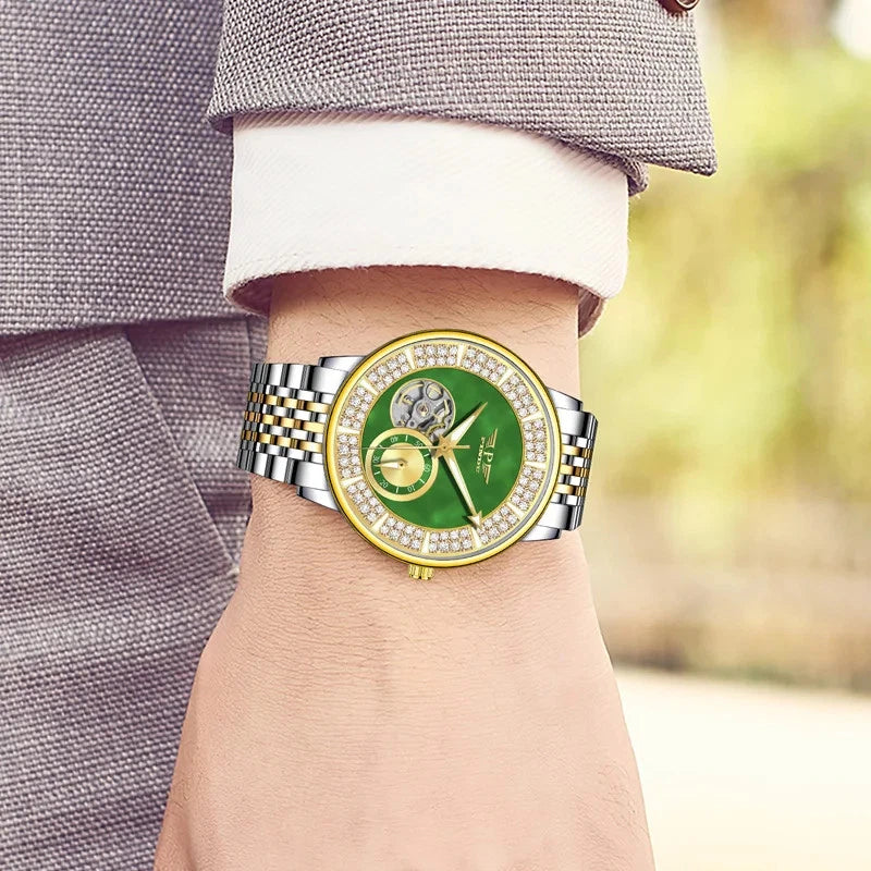 Luxury watch with green face and silver case on a wrist, blurred background