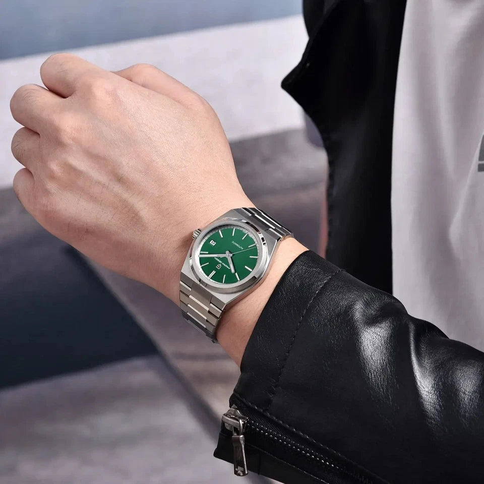 Person wearing a watch with a green face and silver case, set against a blurred background.