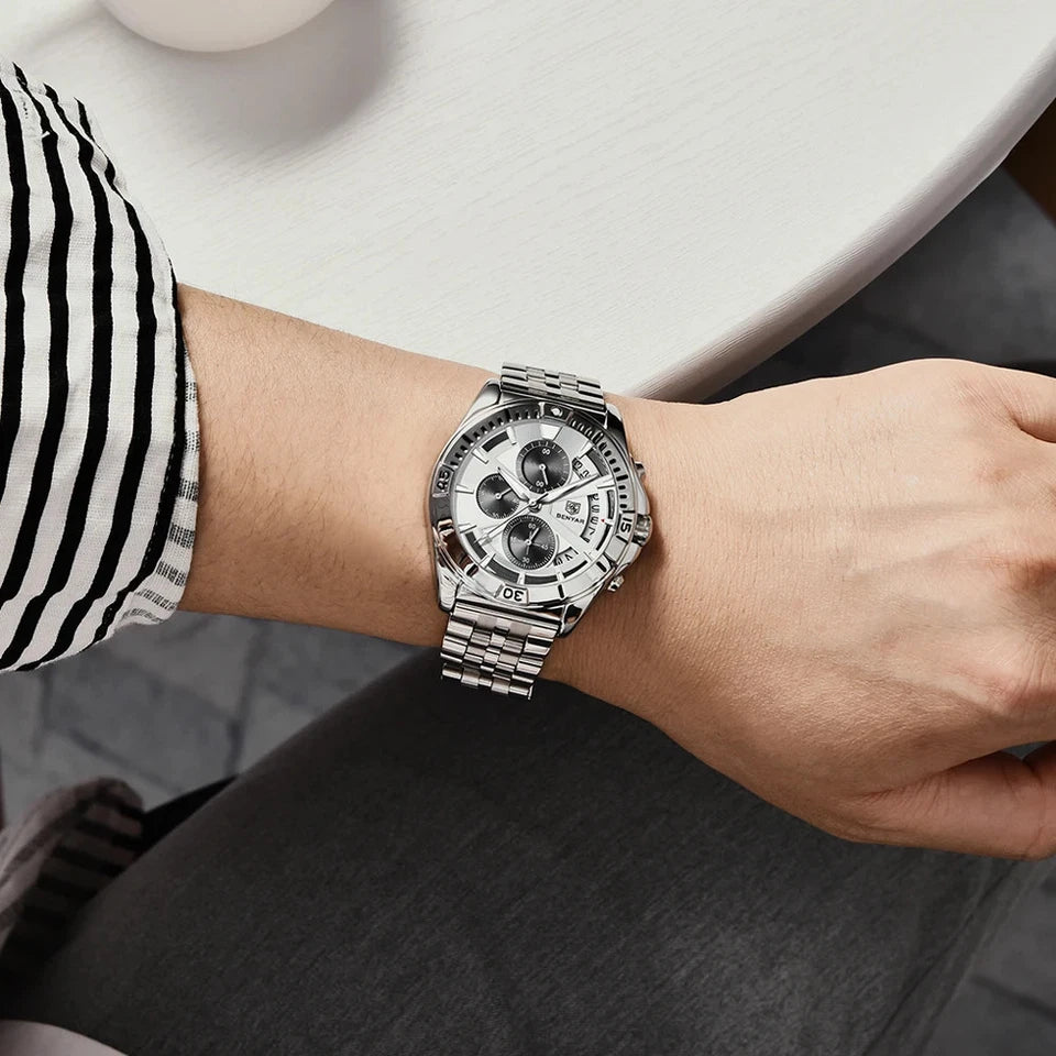Person wearing a silver wristwatch with a detailed face on a neutral background