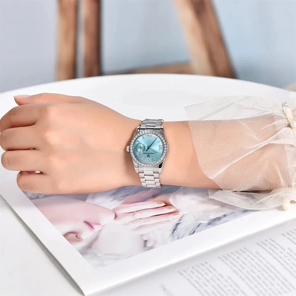Hand wearing a silver watch with a blue face on a white surface