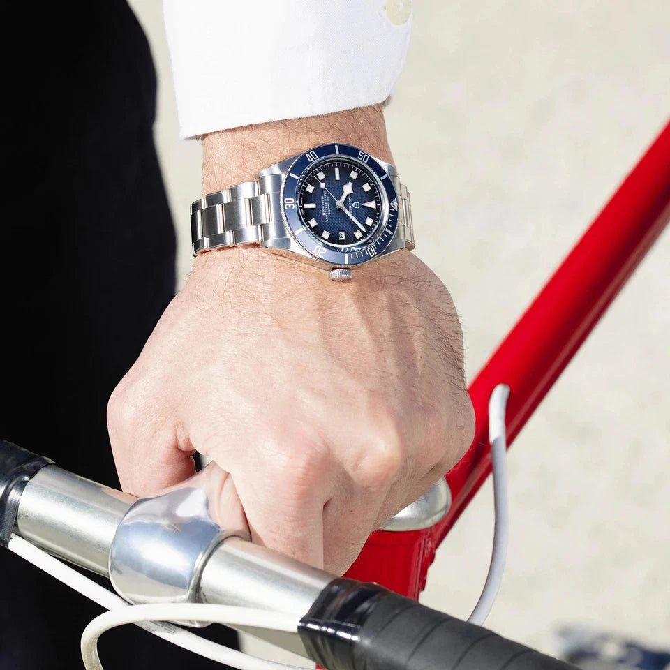 Hand wearing a silver watch with a blue face on a red bicycle handlebar.