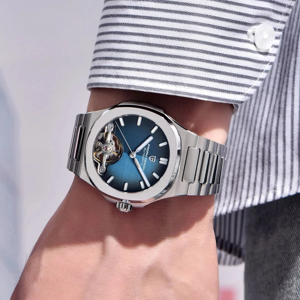 Silver watch with a blue face on a wrist, wearing a striped shirt.