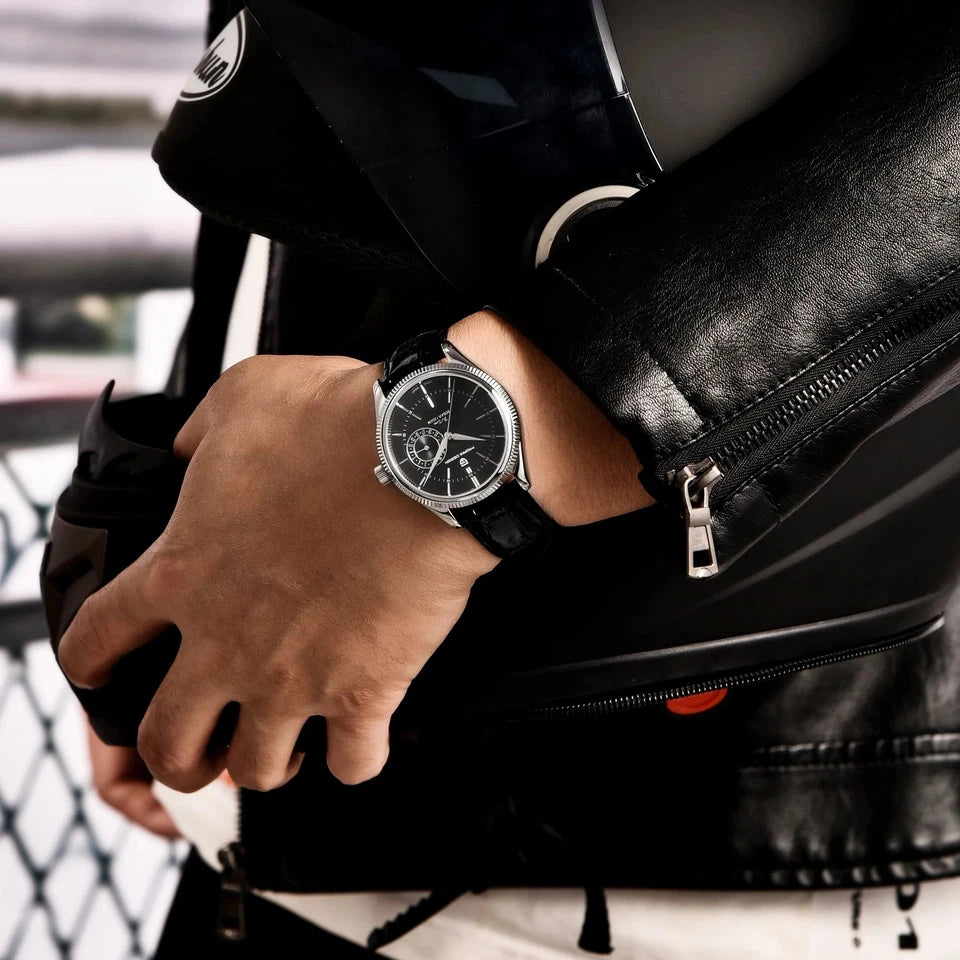 Person wearing a black leather jacket and watch, with a blurred background