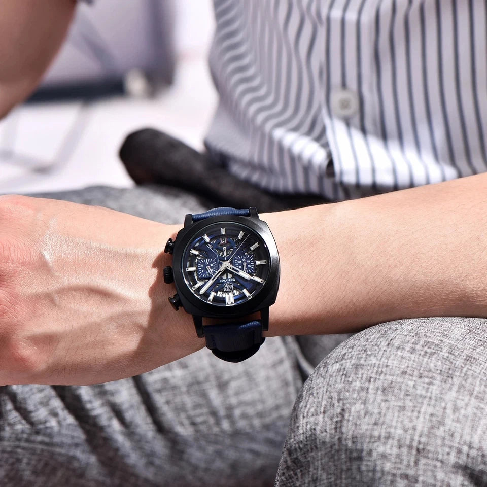 Person wearing a black wristwatch with a detailed face on a blurred background