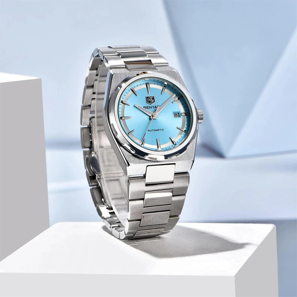 Silver watch with a blue face on a white platform against a light blue background