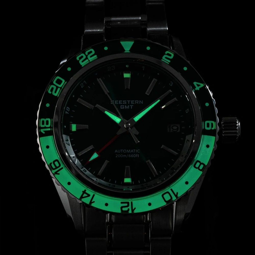 Seestern S456 GMT dial and bezel glowing blue-green lume in the dark with red GMT hand, close-up