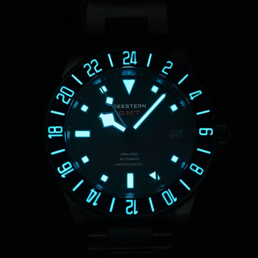 Seestern S462 titanium GMT black dial and bezel glowing blue-green lume in the dark, front close-up